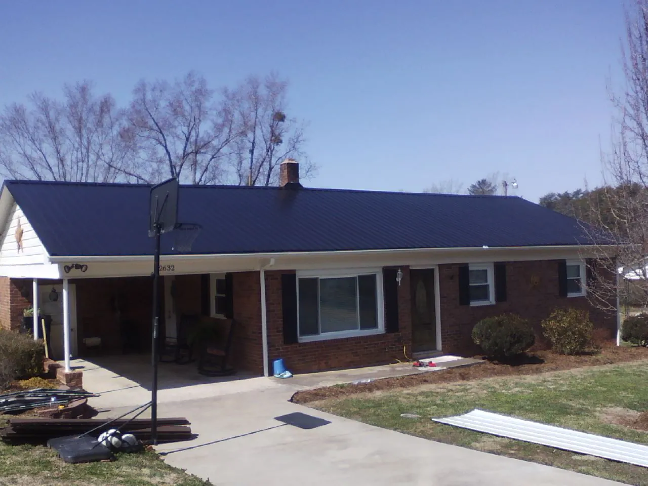 Finished dark blue metal roof on a brick ranch with a carport in Warsaw