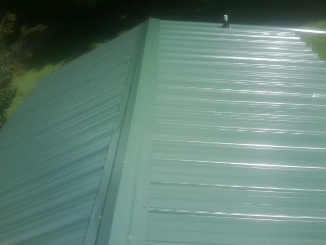 New green metal panels meeting at the ridge of a roof — Flat Roof Repair work by our crew in Warsaw