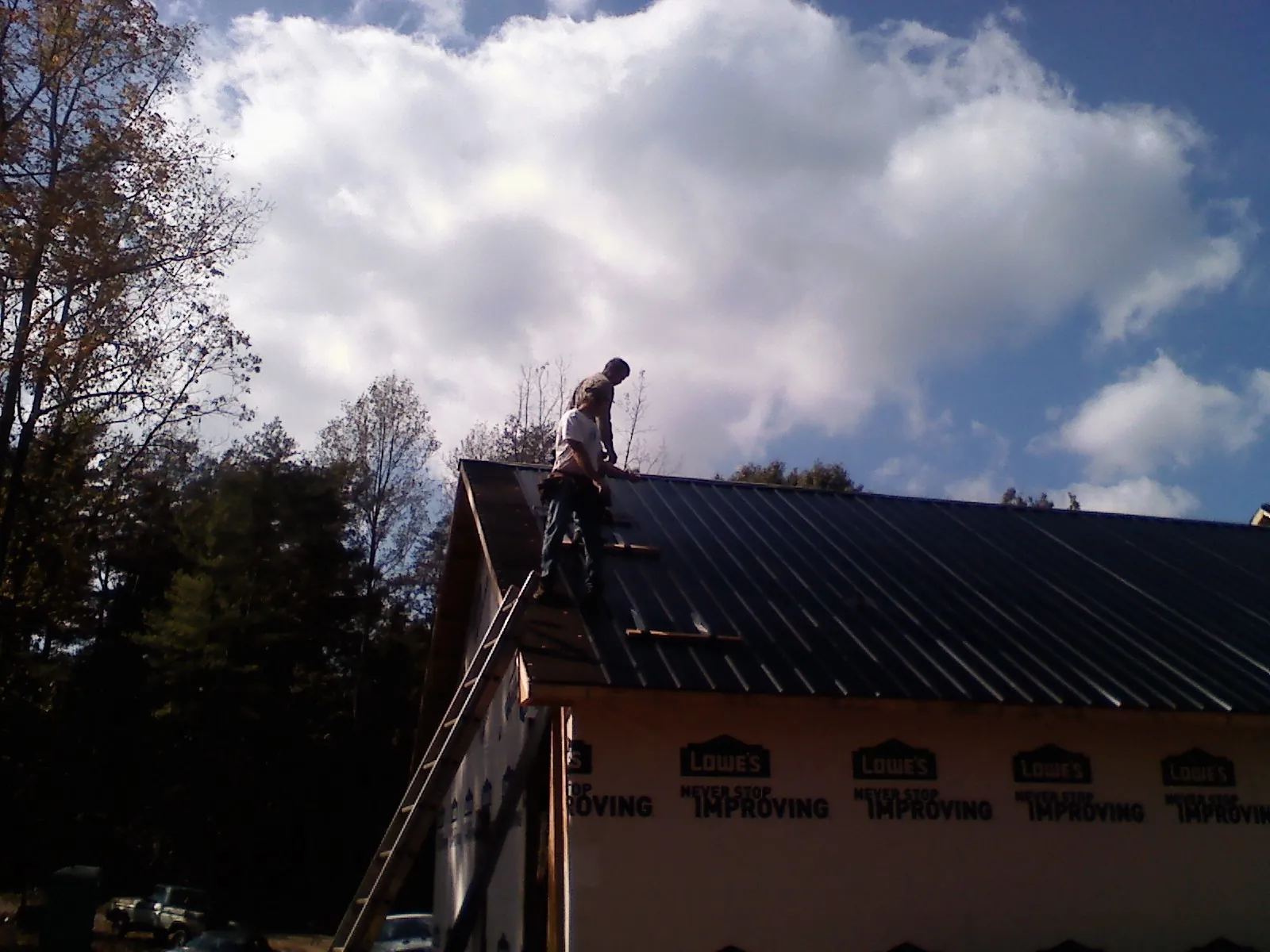 Roofer fastening dark metal panels high against a cloudy sky, from a Roof Inspection job in Warsaw